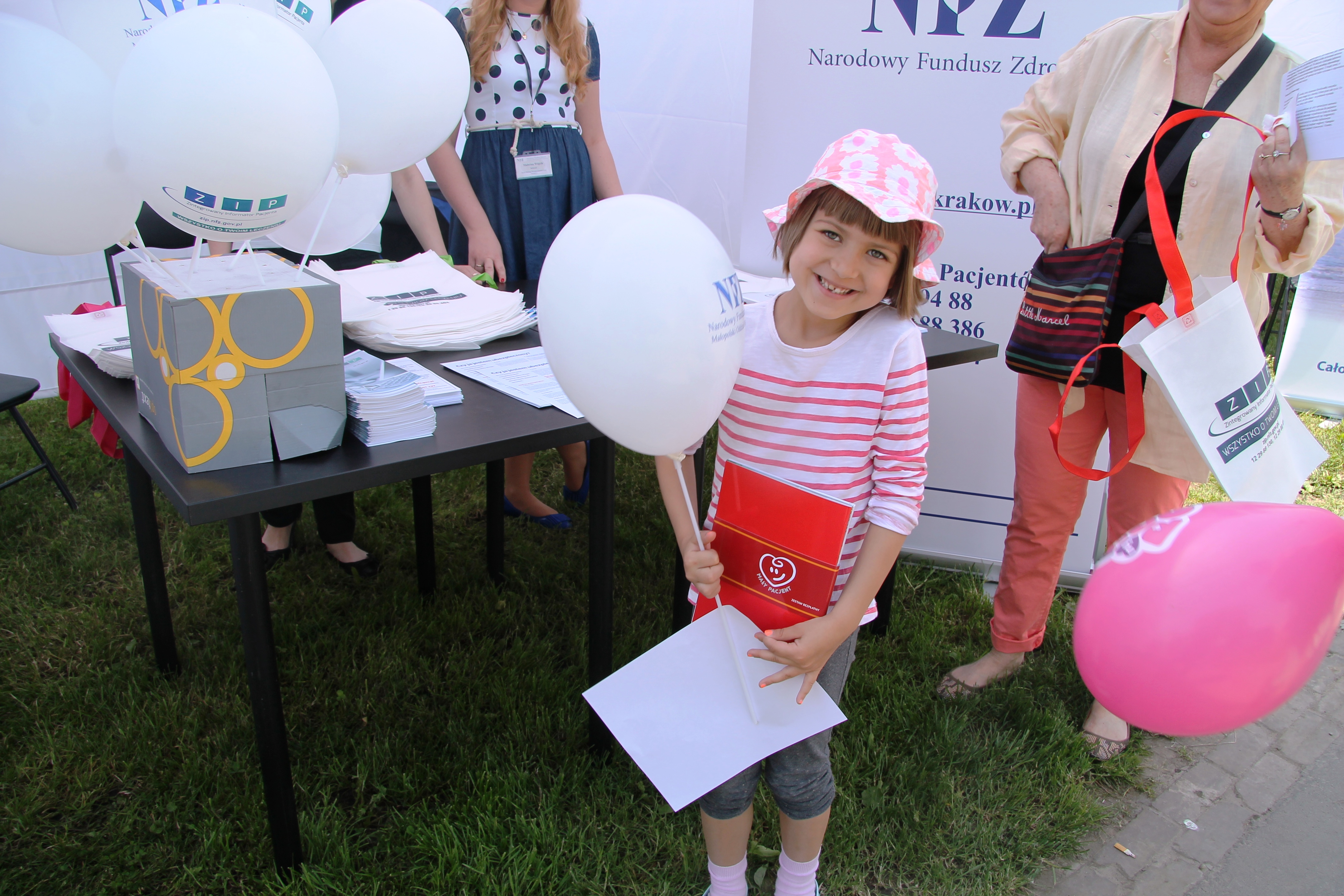 Stoisko NFZ, uśmiechnięta dziewczynka trzyma balonik z logo NFZ